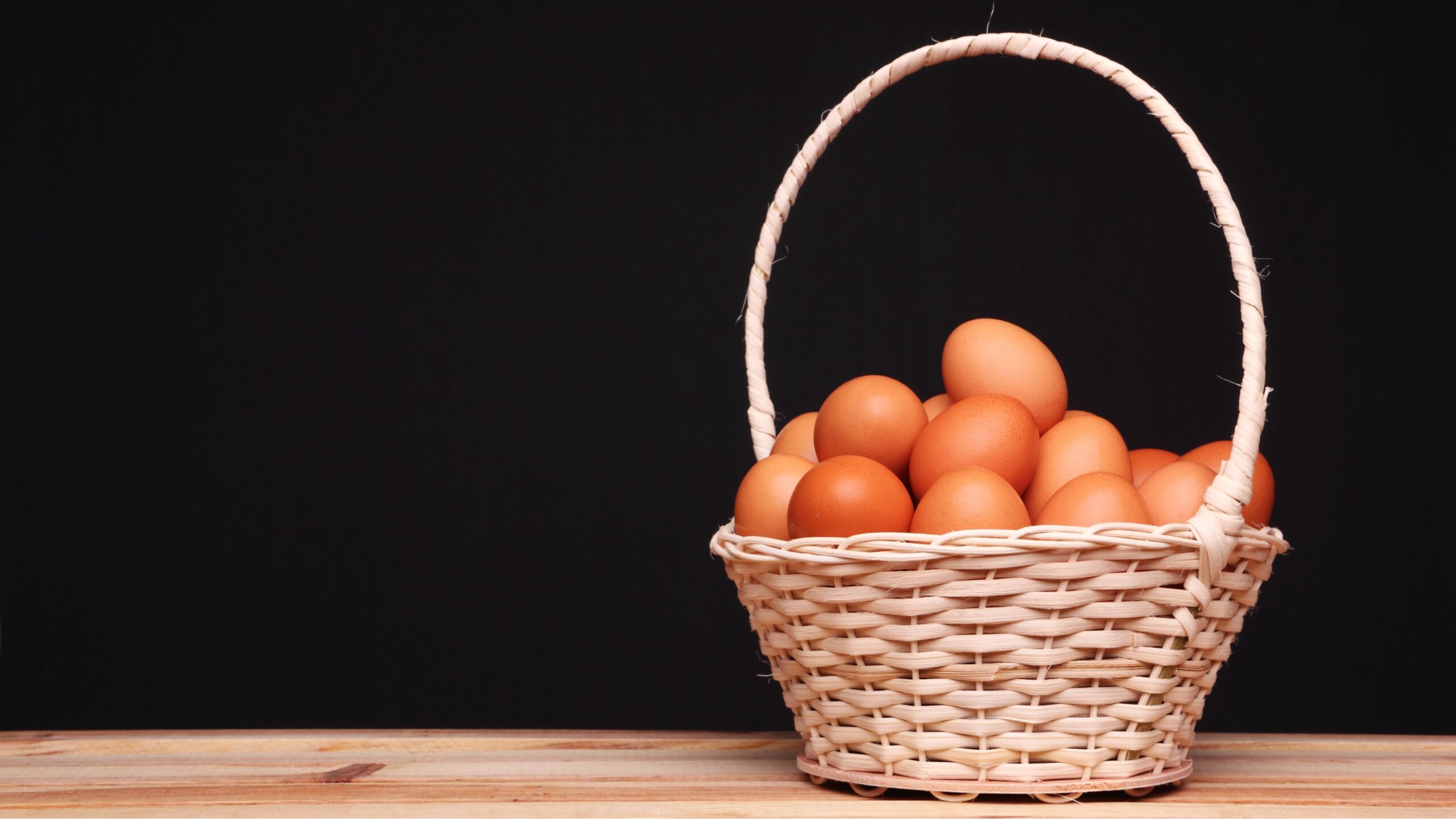 Black background with a basket, containing eggs. on a wooden table