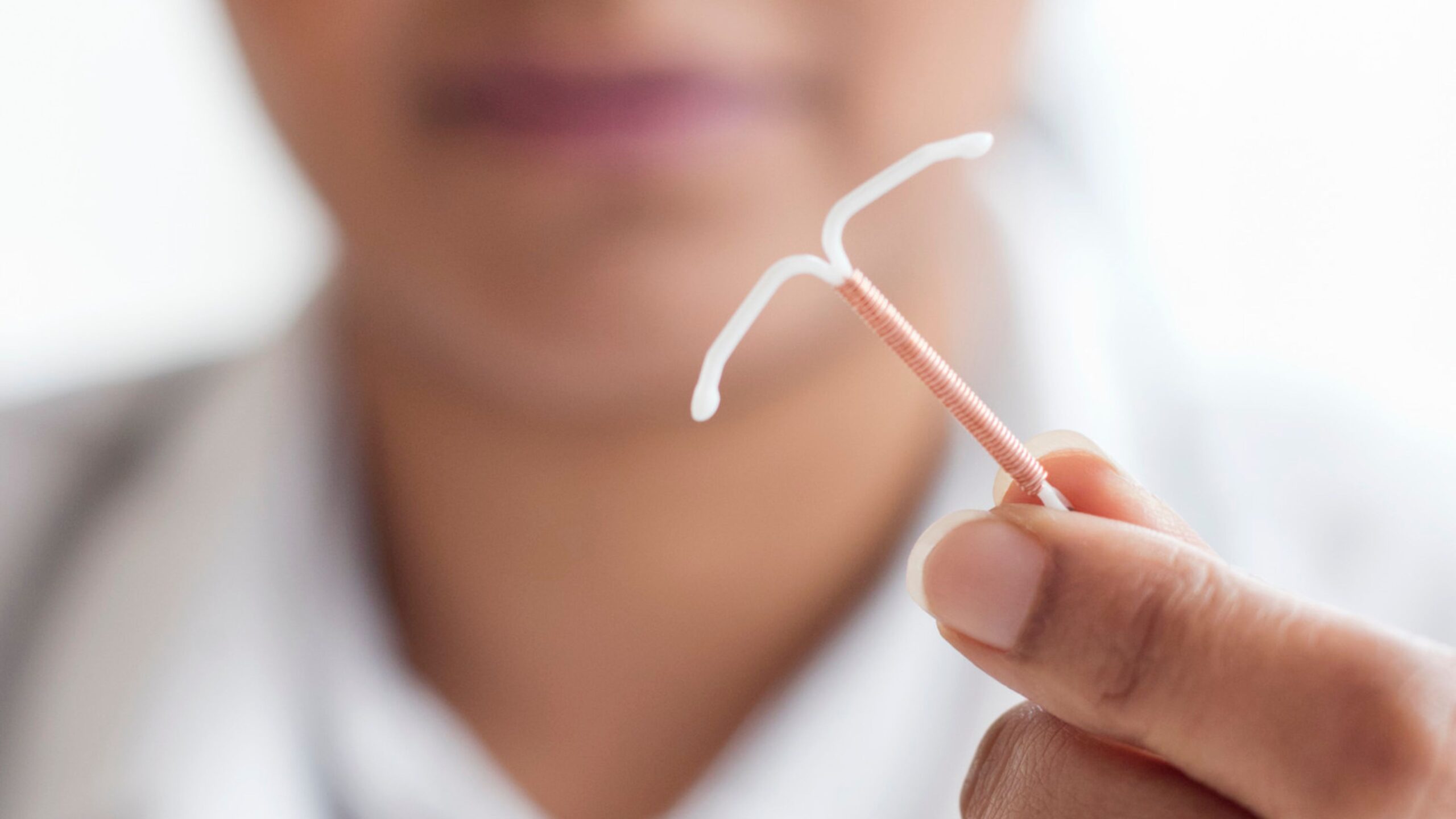 women's face faded in the background while she holds an IUD in one hand.