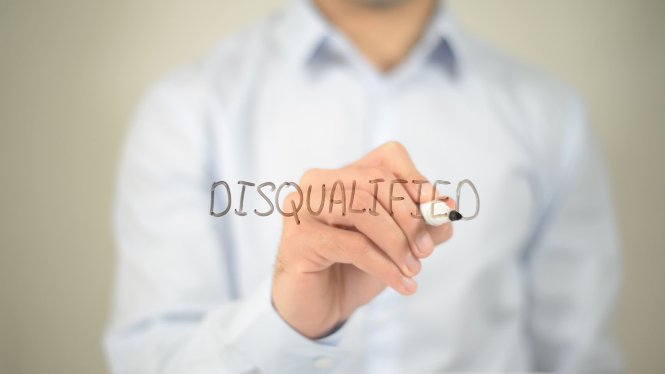 Man in a collared shirt writing the word "disqualified" on a mirror with black marker