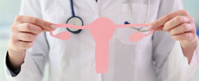 A doctor in a white lab coat holding up a pink paper cut out of the female reproductive system.