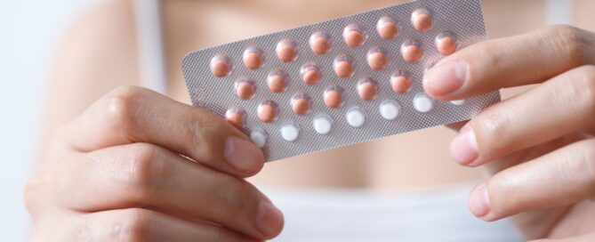 Woman out of focus, holding birth control pills close to the camera.